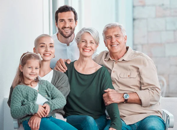 Cute little girl sitting on the couch together with family. Happy child sitting with her parents and grandparents at home. Caucasian family smiling while relaxing together during a visit.
