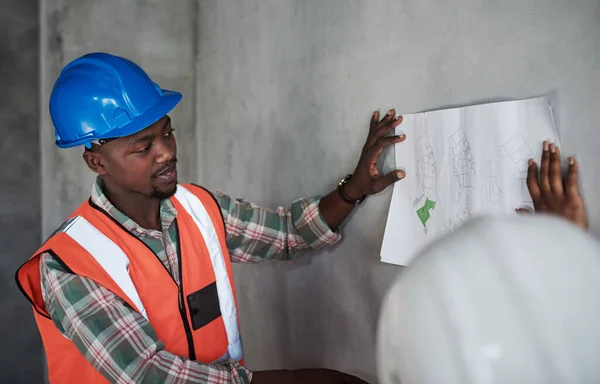 Teamwork makes the construction project work. a young man and woman going over building plans at a construction site