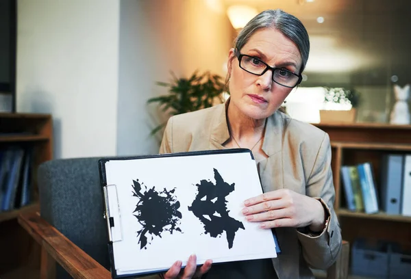What do you see when you look at this picture. Portrait of a mature psychologist holding up an inkblot test during a therapeutic session
