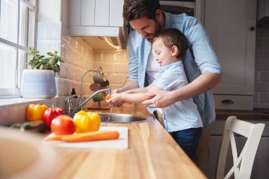 Yemek hazırlamanın ilk adımı. Küçük bir çocuk ve babası evde sebze yıkıyorlar.