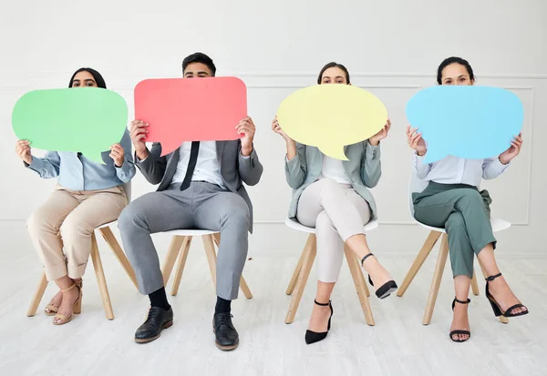 Let your voice be heard. Portrait of a group of businesspeople holding speech bubbles while sitting in line against a grey background