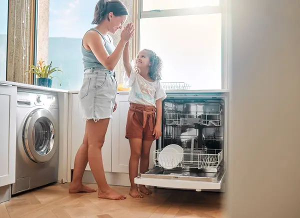 小さな女の子は母親が家で家事をするのを手伝っています ハッピーママと娘は 食器洗い機を一緒に荷を下ろしながら 高い5を与えています タスクを行うことによって責任を負うことを学ぶ子供 — ストック写真