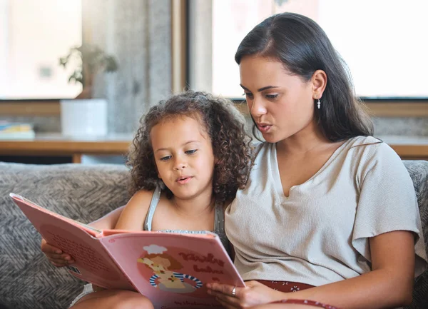 ヒスパニック系の母親と娘を愛し 自宅に座ってストーリーブックを読んでいます 教える 小さな 女の子 ながら ソファ — ストック写真