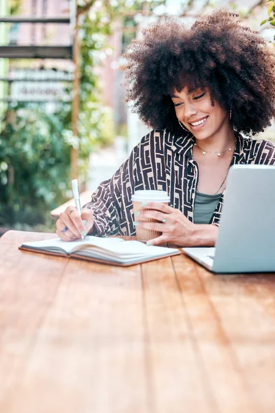 年轻而快乐的混合种族女商人 卷曲的黑人在写日记 喝咖啡 坐在咖啡店外面的笔记本电脑上工作 在餐馆学习的西班牙女生 — 图库照片