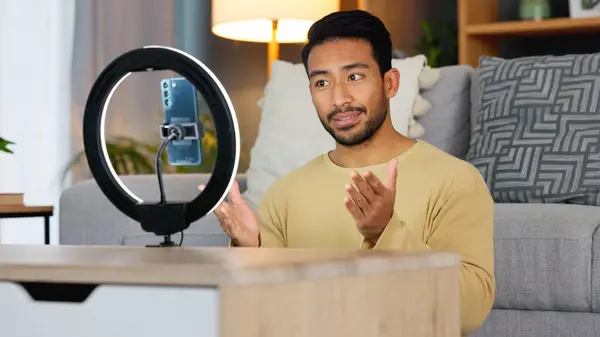 Influencer man, phone and ring light for live stream, web chat or recording in home living room. Content creator guy, video call or vlogger on smartphone, contact or communication in lounge at house.