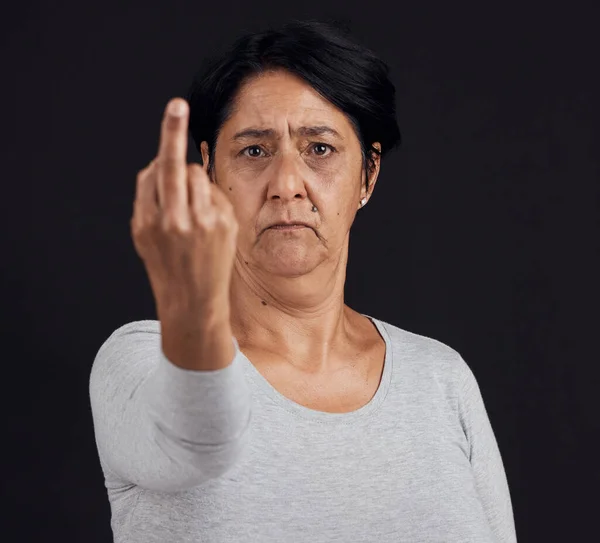 Portrait, reject and senior woman with middle finger, opinion and angry expression on a black studio background. Face, female person or elderly model with hand gesture, rude and frustrated with anger.