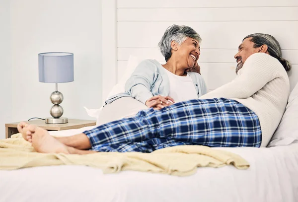 Love, relax and an elderly couple in bed together, bonding in the morning while enjoying retirement in their home. Happy, conversation and an old woman with her husband in a bedroom while on holiday.