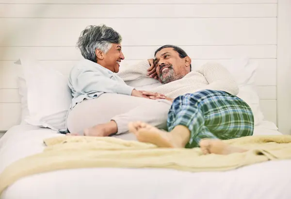 Talking, happy or old couple in bedroom to relax, enjoy romance or morning together at home. Holding hands, senior woman or elderly man laughing or bonding with love, support or smile in retirement.