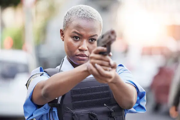 Gun, serious and female police officer in the city for an arrest to stop crime in a street. Upset, young and African woman security guard with pistol for safety, authority and law enforcement in town.