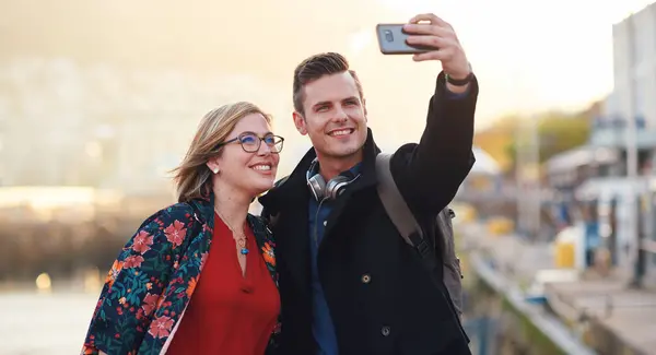 Selfie, travel and couple with phone by harbor enjoying vacation, holiday and honeymoon in Amsterdam. Journey, adventure and happy people take picture for social media, post and memory on smartphone.