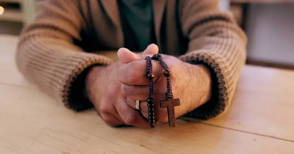 Hands, rosary and cross with closeup for religion, peace and hope at desk, home or praying for worship. Person, crucifix and jewelry for faith, mindfulness and connection to holy spirit, Jesus or God.