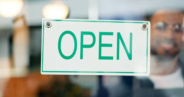 Storefront, small business or open sign on window in coffee shop or restaurant for service or advertising. Man, portrait or entrepreneur holding board, poster or welcome for message in cafe or diner.