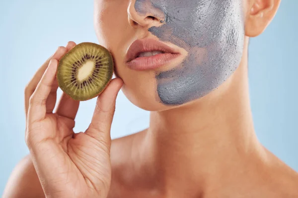 Fruit, face mask and woman with kiwi for organic skincare or cosmetic treatment isolated in a blue studio background. Skin, beauty and young female person with facial wellness, nutrition and detox.