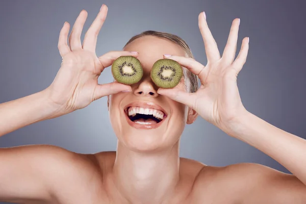 Kiwi, woman and cover eyes for beauty, skincare and wellness food on studio background. Happy model, smile and organic green fruits for natural cosmetics, detox and nutrition benefits of funny face.