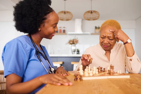 Black people, nurse and thinking in elderly care for chess, fun or social activity together at home. African medical professional playing strategy board game with senior female person in the house.