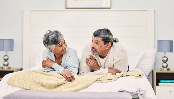 Talking, morning or old couple in bedroom to relax, enjoy holiday or vacation together at home. Conversation, senior woman or elderly man speaking or bonding with love, trust or support in retirement.