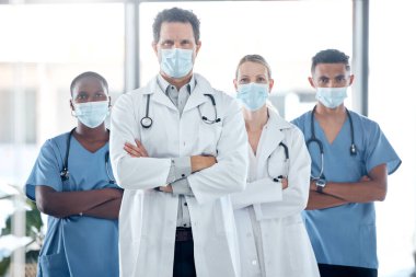 Doktor, hemşire ve liderlik. Tıp hastanesinde kollarını kavuşturarak takım güvenliği için maske takmış. Gururlu, profesyonel ve motive olmuş sağlık çalışanları klinikte birlikte savaşıyorlar..