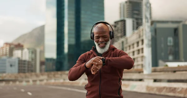 Man, music and smart watch in city for exercise, fitness performance and workout results. Happy senior african runner check timer, clock and healthy training progress with headphones in urban road.