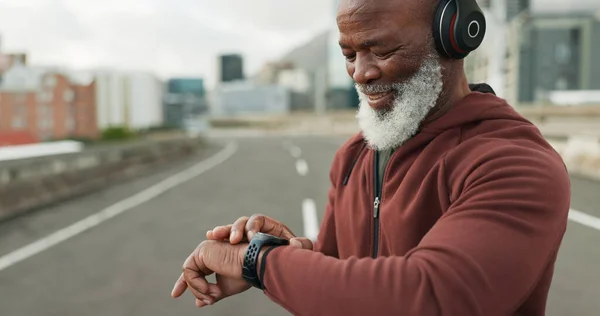 Man, music and smart watch in city for workout, cardio performance and exercise results. Happy senior african runner, sports gear and timer for clock, healthy training progress and headphones in road.