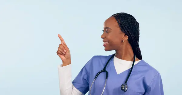 Smile, information and a nurse black woman pointing to space in studio on a blue background for healthcare. Medical, presentation and checklist with a happy young medicine professional showing mockup.