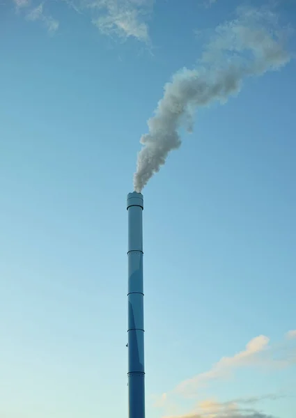 A factory chimney with smoke billowing into the air. Large amounts of steam or smoke billowing from an industrial smoke stack, adding to pollution and air contamination from big industrial industries.