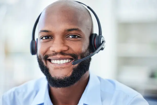 Portrait of male call center agent with a headset working in a corporate office doing crm. Cheerful, young and African ecommerce customer service representative or support hotline operator at work