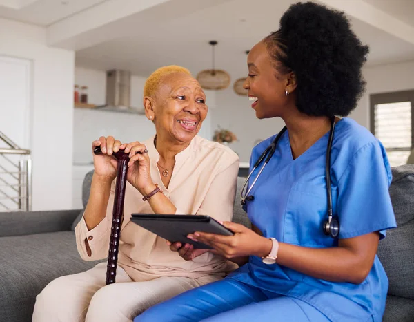 Health consultation, nurse and black woman with tablet for medical information or advice online. Smile, conversation and an African nurse helping a senior patient with healthcare on an app in a house.