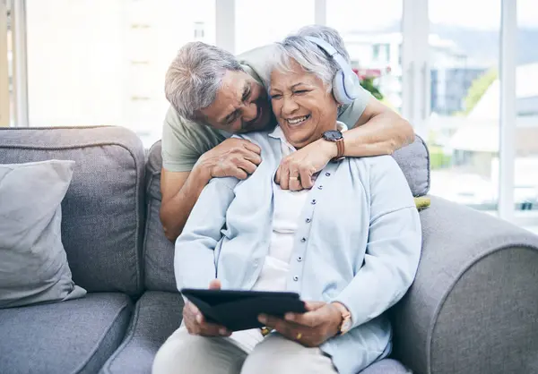 Laughing, hug and couple with a tablet for a website, streaming music or a podcast together. Love, embrace and a senior man and woman with a movie or funny video on technology or listening to audio.