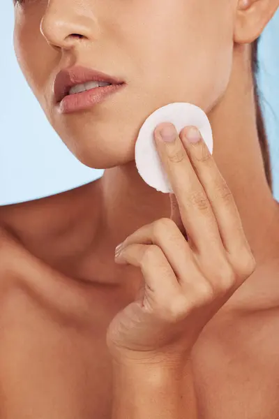 Woman, hands and cotton pad for skincare, makeup removal or cosmetics against a blue studio background. Closeup of female person with round swab or patch for cleaning, hygiene or facial spa treatment.