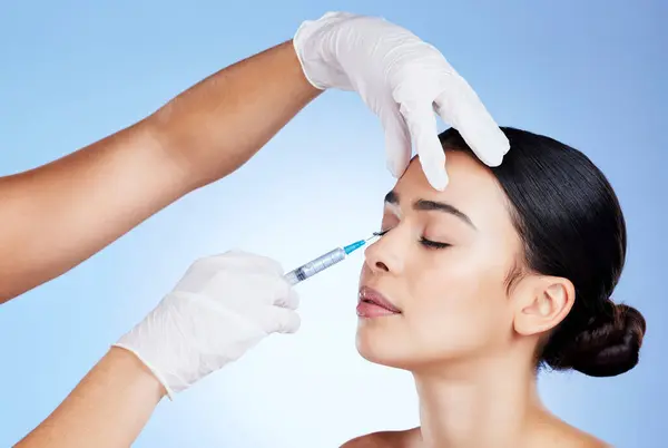Plastic surgery, face and surgeon injection for beauty, filler and change for a woman in studio. Aesthetic model and doctor hands for cosmetic surgery, transformation or dermatology blue background.