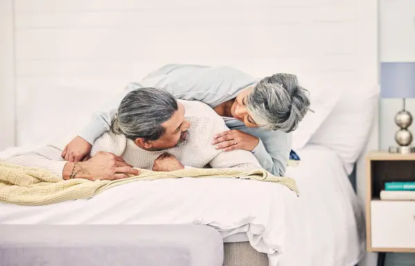 Senior couple, laugh and play on bed in home, hotel and happy together with romance, game and comic joke. Elderly woman, old man and funny on vacation, holiday and relax in bedroom, bonding and love.