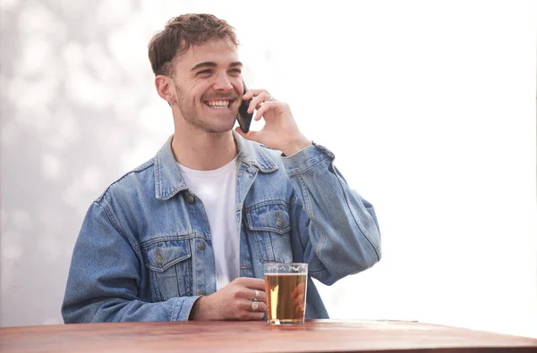 Beer, alcohol and phone call communication for man talking, discussion and speaking to 5g mobile contact. Conversation, shop service and happy gen z person relax with glass drink at outdoor pub table.