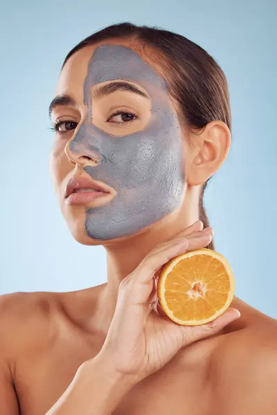Portrait, face mask and orange with beauty and skincare, eco friendly product and cosmetic on blue background. Charcoal facial, citrus fruit and vitamin c, female model has skin detox and dermatology.