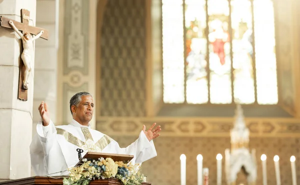 Religion, Christianity and priest speaking in church with arms raised standing by podium. Ceremony, mass and religious leader in worship, preaching and prayer for congregation in spiritual building.