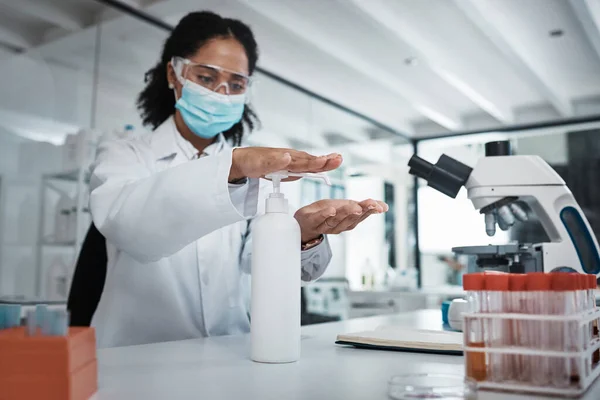 Science, covid or sanitizer with a doctor black woman at work in a laboratory to sterlize her hands. Medical, health and safety with a female scietist working in a lab for research or innovation.