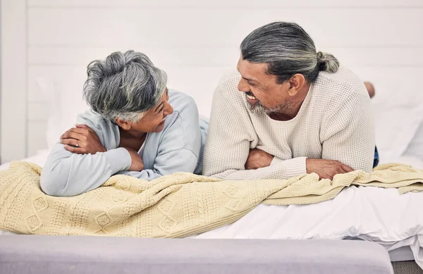 Laughing, talking or old couple in bedroom to relax, enjoy conversation or morning together at home. Speaking, happy senior woman or funny elderly man bonding with love, joke or smile in retirement.