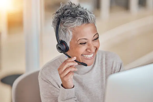 Computer, smile and a senior woman in a call center for customer service, support or assistance online. Contact, headset and a happy female consultant working at a desk in her professional crm office.