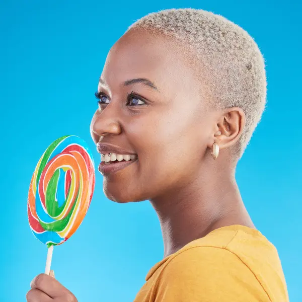 Lollipop, thinking and a woman with candy in studio for sweets, rainbow and creative idea. Profile of happy black female person isolated on a blue background with sugar, freedom and smile or color.
