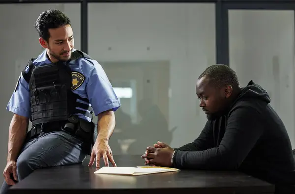 Police, interrogation and black man, suspect or criminal investigation for crime at station. African person with handcuffs at table, detective and people in discussion, interview and law questions