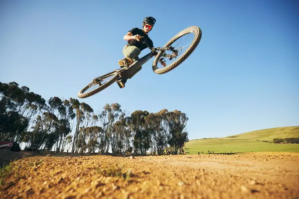 Jump, mountain bike and man outdoor in nature for extreme sports, training or workout. Sky, air or wellness of male person with courage or bicycle stunt for off road cycling, travel or adventure.