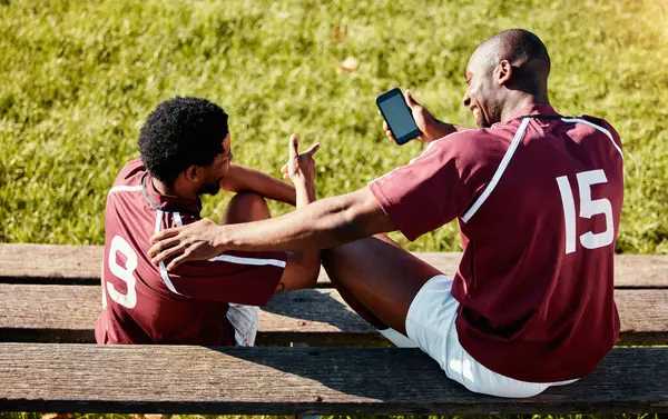 Rugby, teamwork and phone with sports man friends sitting on the bench during a game outdoor. Sport, fitness or social media with a male athlete and friend taking a break from training to rest.