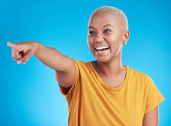 Pointing, smile and black woman with advertising space, happiness and announcement on a blue studio background. Happy girl, female person and model with gesture, direction and choice with a decision.