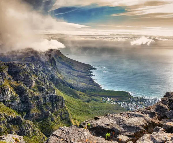 Aerial view of clouds rolling over Table mountain in Cape town, South Africa with copyspace. Beautiful landscape of green bushes and rocky terrain on misty morning, calming view of the ocean and city.
