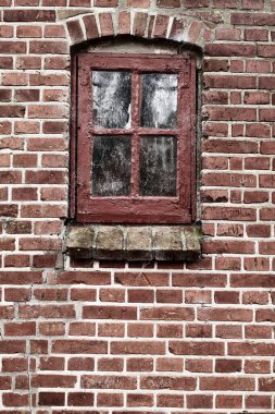 Old dirty window in a red brick house or home. Ancient casement with red wood frame on a historic building with clumpy paint texture. Exterior details of a windowsill in a traditional town or village.