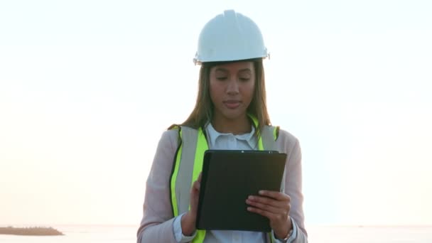 現場のプロの若い女性建設労働者 基礎を築く前に建築計画を読んでいる専門家の建築インストラクター 日没時の建設レイアウトの企画 — ストック動画