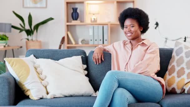 新しい不動産の所有者または不動産投資家として家のリビングルームでリラックスするアフロ女性を笑う 自信を持って 笑顔で野心的な女性の肖像画 購入した家でソファーの快適さを楽しみます — ストック動画