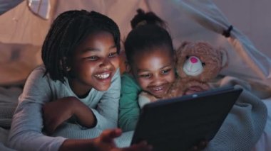 Yatak odası, gece ve tabletli siyah kızlar, çizgi filmli komik ve mutlu ev ve bağlantılı mizah. Kardeşler, çocuklar ve teknolojiye sahip çocuklar, oyuncak ayı ve internetteki online video..