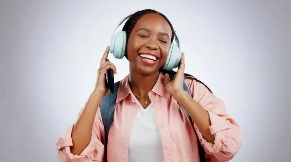 Music, student or happy black woman in studio listening to radio playlist to relax on grey background. Face, headphones or African person with smile singing or streaming a song audio or sound track.