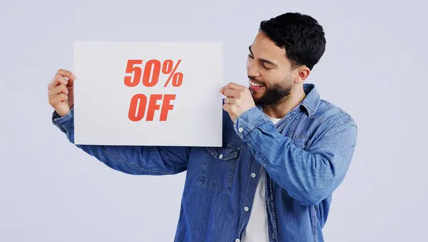 Happy man, sign and sale in discount, promotion or banner against a gray studio background. Male person or model smile with billboard, poster or half price in advertising or marketing for store promo.