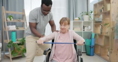Engelli bir kadın, fizyoterapi ve esneme bandı, kas rehabilitasyonu ya da fizik tedavi hizmeti. Tekerlekli sandalyedeki yaşlı hastaya klinik, fizyoterapist ve tıbbi destek.